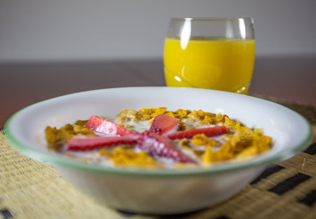 A breakfast set of cereal, orange juice with slice of strawberries with fresh milk 