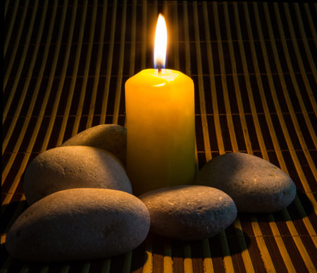 Zen stones and yellow candles on a bamboo matの写真素材