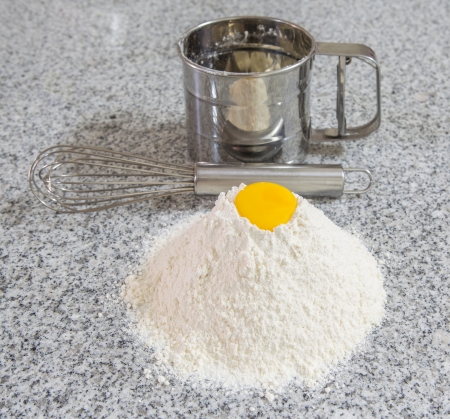 Flour, egg yolk, egg beater and flour sifter on a granite counter surface の写真素材