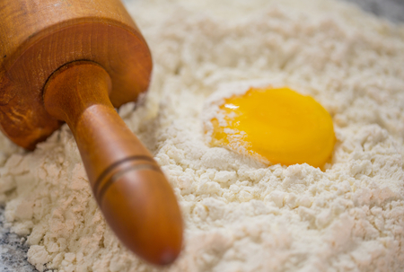 Pastry making preparation with egg, yolk, flour and rolling pin on a granite counter surface の写真素材