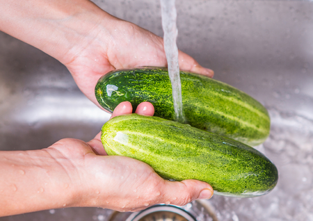 Female hands washing cucumber at the kitchen sink の写真素材
