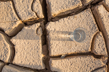 A glass of water on a parched soil during drought and dry season の写真素材
