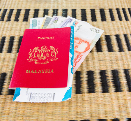 Malaysian passport with Philippine currency and airplane boarding pass on a wicker matの写真素材