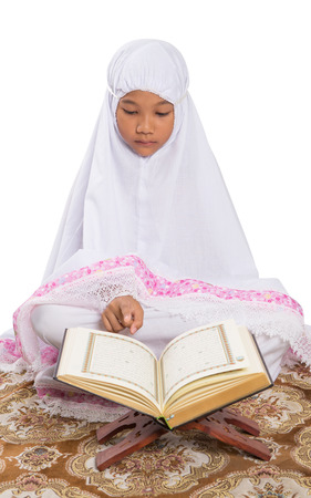 Young Asian Muslim girl reading Al Quran on a prayer mat over white backgroundの写真素材