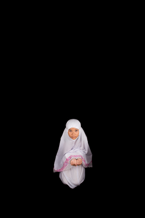 Young Asian Muslim girl in white hijab cupped her hands saying a prayer over black backgroundの写真素材