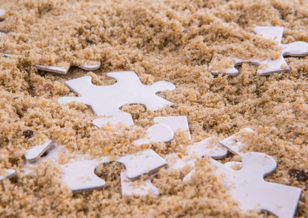 Pieces of white jigsaw puzzle buried in sand