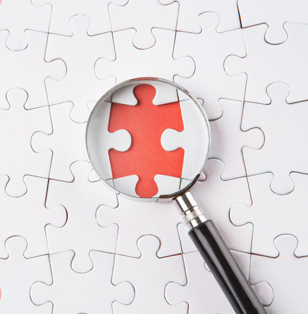 Missing jigsaw puzzle pieces revealing a red surface layer with a magnifying glassの写真素材