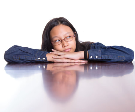 Young Asian Malay girl with her face reflection on a wooden table surface の写真素材