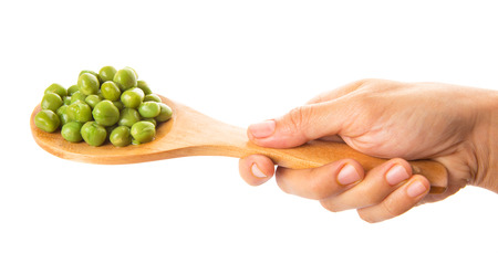 Female hand holding green peas on wooden spoon over white backgroundの写真素材