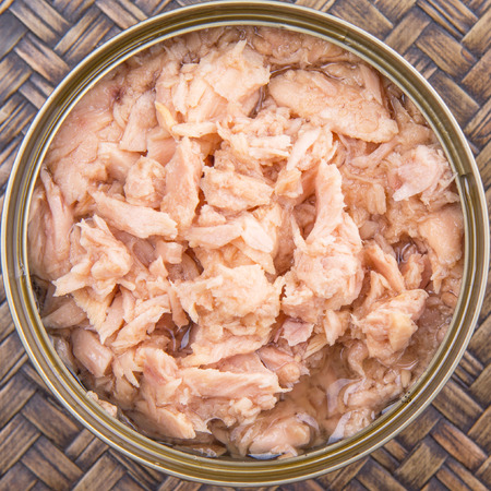 Pieces of canned tuna in a white bowl with a fork on wicker backgroundの写真素材