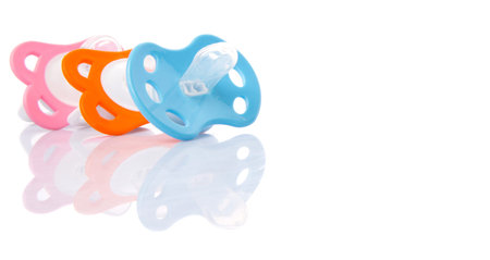 Orange, pink and blue pacifier over white backgroundの写真素材