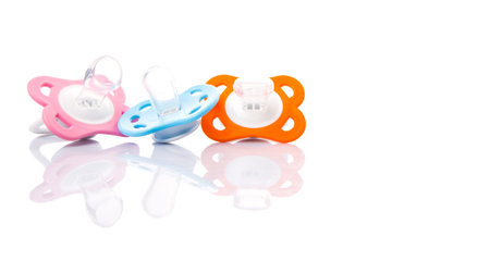 Orange, pink and blue pacifier over white background