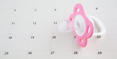 Concept image of baby girl pregnancy delivery due date with calendar page and pink pacifier.