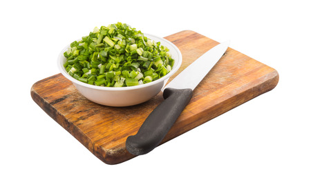 Chopped scallions or spring onion leaves in a white bowl with a cutting knife on a wooden cutting boardの写真素材