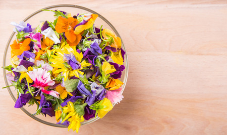 Mix edible flower salad in a glass bowl on wooden cutting boardの写真素材