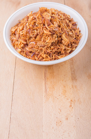 Deep fried shallots for garnishing in white bowl over wooden surfaceの写真素材