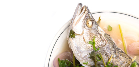 Malaysian dish of sweet and sour steamed barramundi or Asian bass fish on white plate