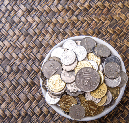 Malaysian coins in a white bowl over wicker backgroundの写真素材