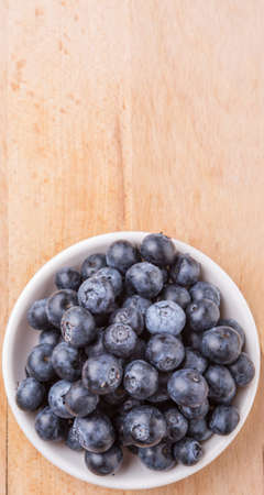 Blueberry fruits in a white bowl on wooden board backgroundの写真素材
