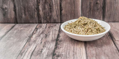 Dried rosemary herb in white bowl on weathered wooden backgroundの写真素材