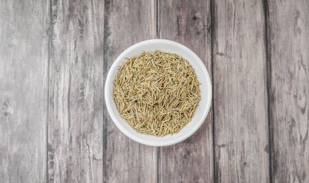 Dried rosemary herb in white bowl on weathered wooden backgroundの写真素材