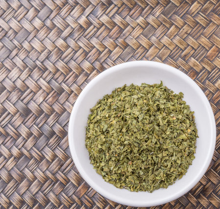 Dried parsley herb in white bowl over wicker backgroundの写真素材