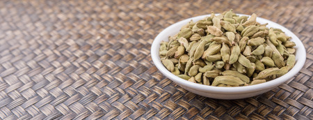 Cardamom spices in white bowl over wicker backgroundの写真素材