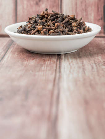 Clove spices in white bowl over weathered wooden backgroundの写真素材