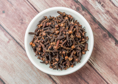 Clove spices in white bowl over weathered wooden background