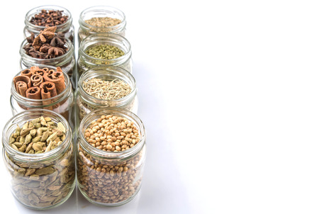 Cardamom, star anise, cinnamon, clove, coriander seed spices and dried bay leaves, parsley, thyme, rosemary herbs in mason jars over white backgroundの写真素材
