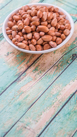 Ground nut or peanuts in white bowl over weathered wooden backgroundの写真素材