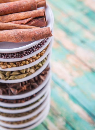 Cardamom, star anise, cinnamon, clove, coriander seed spices and parsley, thyme, rosemary herbs in white bowls over weathered wooden backgroundの写真素材