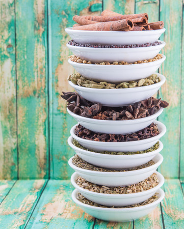 Cardamom, star anise, cinnamon, clove, coriander seed spices and parsley, thyme, rosemary herbs in white bowls over weathered wooden backgroundの写真素材