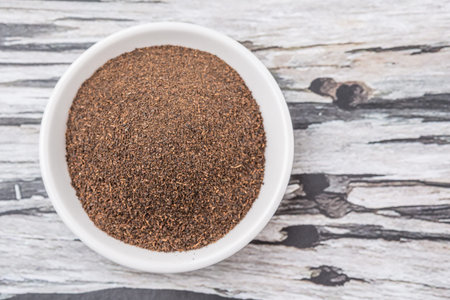 Dried processed tea leaves in white bowl over rustic weathered wooden background