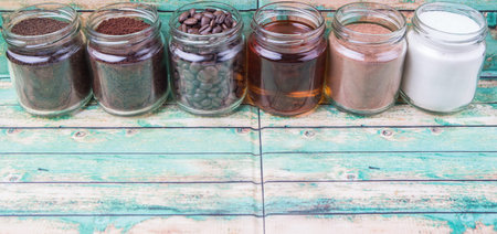 Coffee beans, coffee powder, creamer, cocoa powder, honey and processed tea leaves in mason jars over weathered wooden backgroundの写真素材