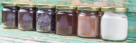 Coffee beans, coffee powder, creamer, cocoa powder, honey and processed tea leaves in mason jars over weathered wooden backgroundの写真素材