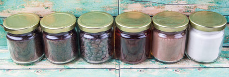 Coffee beans, coffee powder, creamer, cocoa powder, honey and processed tea leaves in a mason jar over weathered wooden backgroundの写真素材