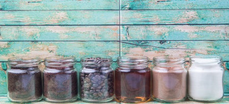Coffee beans, coffee powder, creamer, cocoa powder, honey and processed tea leaves in mason jars over weathered wooden backgroundの写真素材