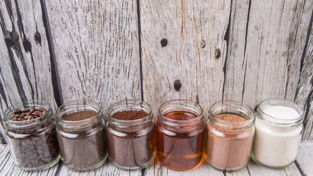 Coffee beans, coffee powder, creamer, cocoa powder, honey and processed tea leaves in mason jars over weathered wooden backgroundの写真素材
