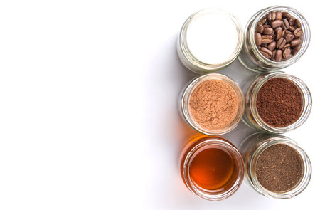 Coffee beans, powdered coffee, honey, chocolate powder and processed tea leaves beverages in mason jar  over white backgroundの写真素材