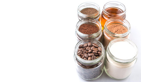 Coffee beans, powdered coffee, chocolate powder and processed tea leaves beverages in white bowls over white backgroundの写真素材
