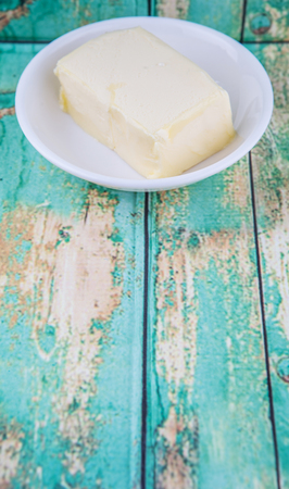 A block of butter in white bowl over rustic wooden backgroundの写真素材