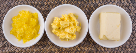 A block of butter, margarine and ghee in white bowls over wicker backgroundの写真素材