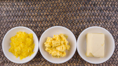 A block of butter, margarine and ghee in white bowls over wicker backgroundの写真素材