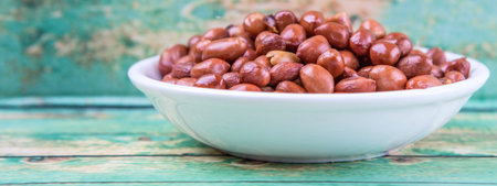 Deep fried peanuts in white bowl over rustic wooden background