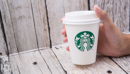 PUTRAJAYA, MALAYSIA - JULY 20TH, 2015. Female hand holding Starbuck coffee paper cup over wooden background. Founded in 1971, Starbucks is the largest coffeehouse company in the world.のeditorial素材