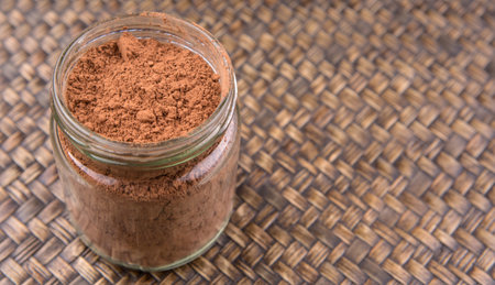 Brown pure cocoa powder in a mason jar over wicker background