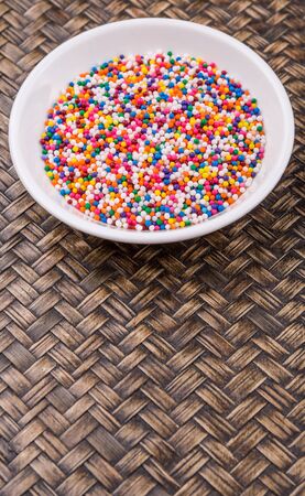 Colorful sprinkle confetti in a white bowl over wicker backgroundの写真素材