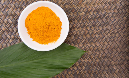 Turmeric powder and turmeric leaves in white bowl over wicker backgroundの写真素材