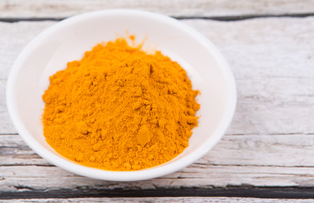 Turmeric powder in white bowl over rustic wooden backgroundの写真素材